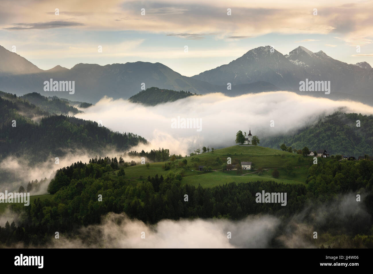 Rollende Nebel bei Sonnenaufgang in den Skofjelosko Hügeln mit St. Thomas Kirche mit Kamnik Savinja Alpen in der Nähe von Ljubljana Slowenien Stockfoto