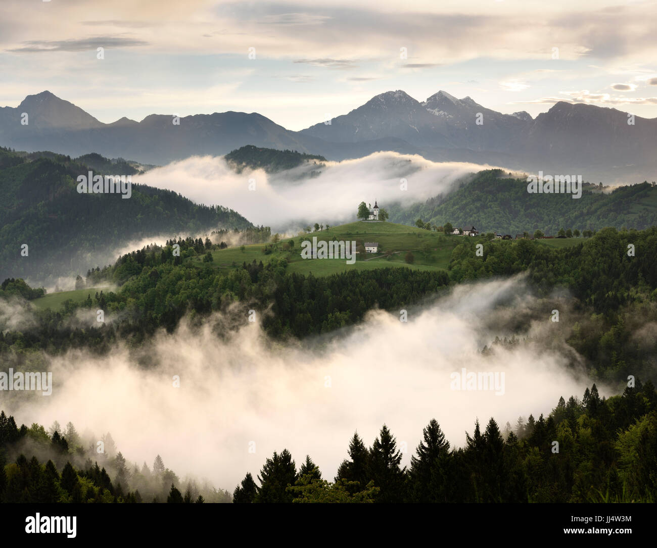 Sanften Nebel bei Sonnenaufgang mit Bergen von Kamnik Savinja Alpen Skofjelosko Hills mit St. Thomaskirche in der Nähe von Ljubljana Slowenien Stockfoto