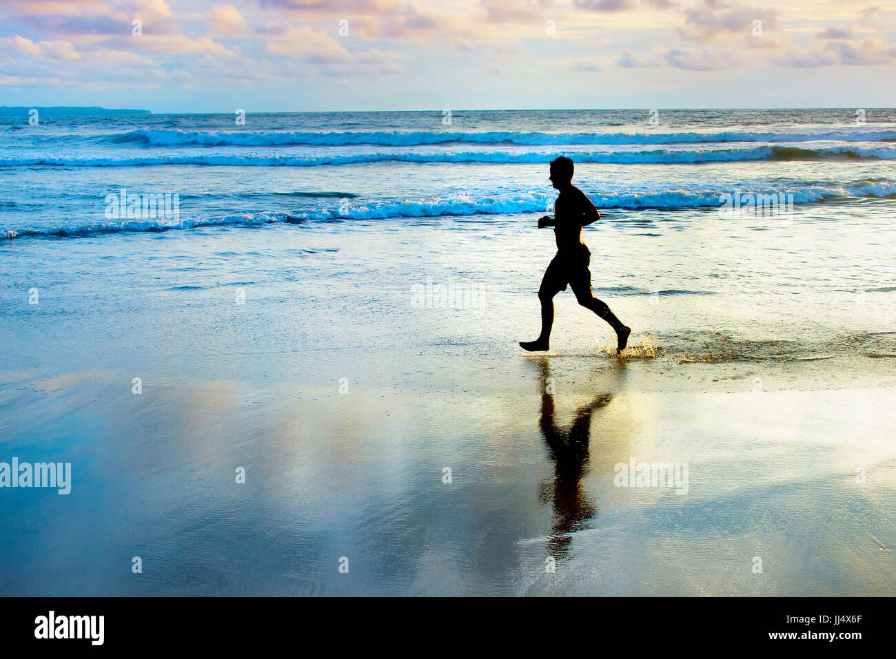 Mann, jogging am Strand bei Sonnenuntergang. Insel Bali, Indonesien Stockfoto