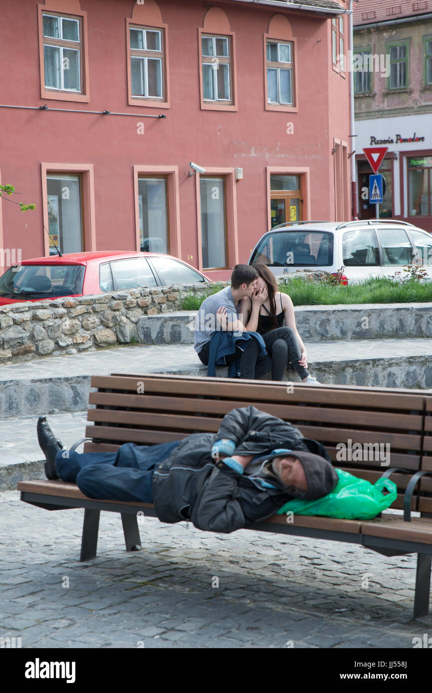 Eine Obdachlose schlafen auf einer öffentlichen Bank in Sibiu während zwei Jugendliche sind Küssen, Siebenbürgen, Rumänien Stockfoto