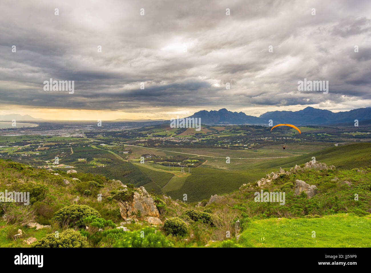 Gleitschirm fliegen über die grünen Berge rund um Cape Town, Südafrika. Wintersaison, bewölkt und dramatischen Himmel. Nicht erkennbare Personen. Stockfoto