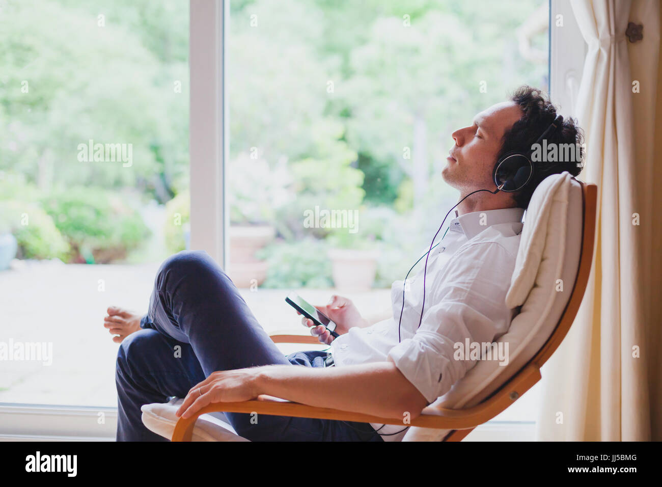 hören entspannende Musik zu Hause, entspannt Man Kopfhörer sitzen im Liegestuhl im modernen hellen Innenraum Stockfoto