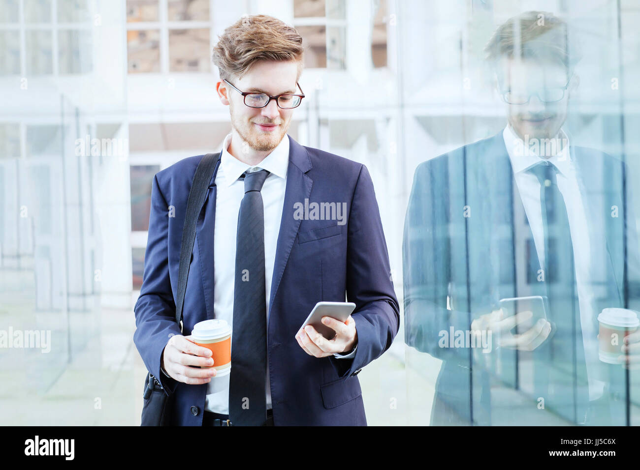 Geschäftsmann mit Smartphone und trinken Kaffee im modernen hellen Innenraum des Büro Glaskorridor Stockfoto