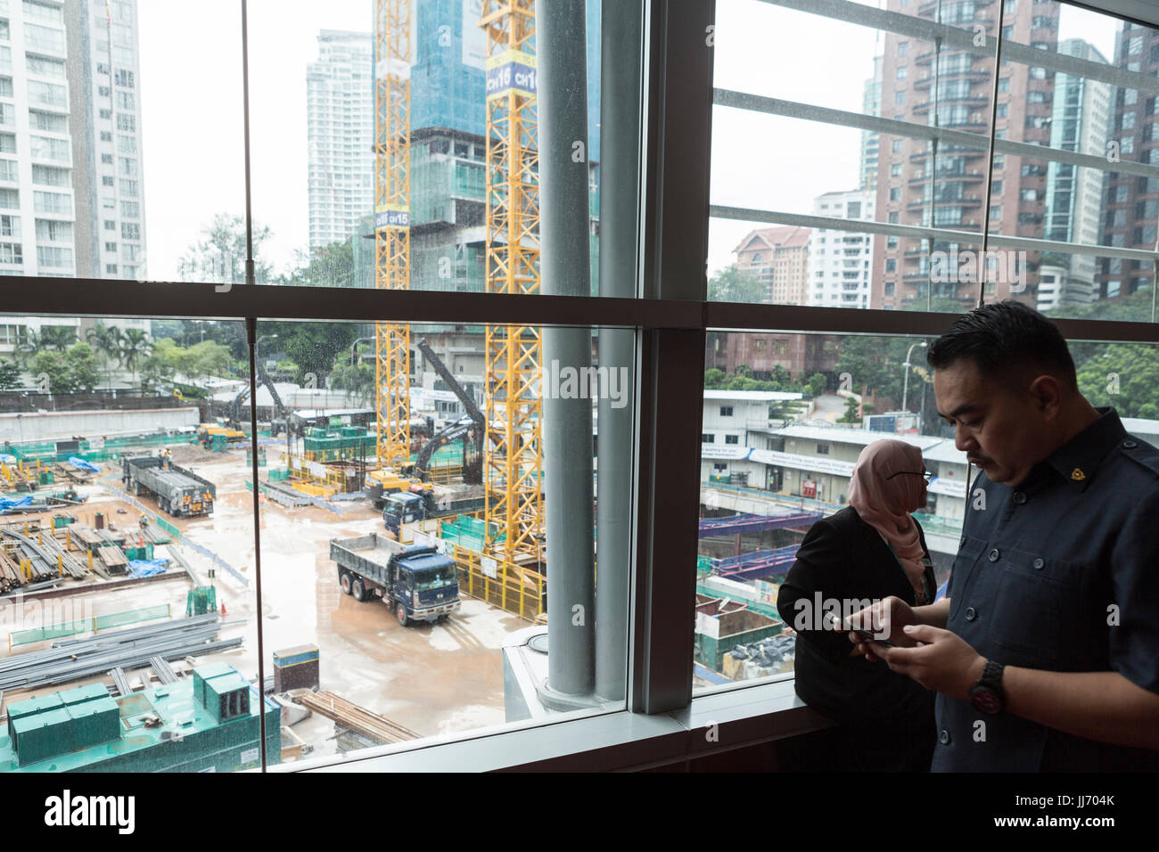 Eine Baustelle ist durch ein Fenster gesehen, wie ein Mann am Telefon im Kuala Lumpur Convention Center in Kuala Lumpur, Malaysia spricht Stockfoto