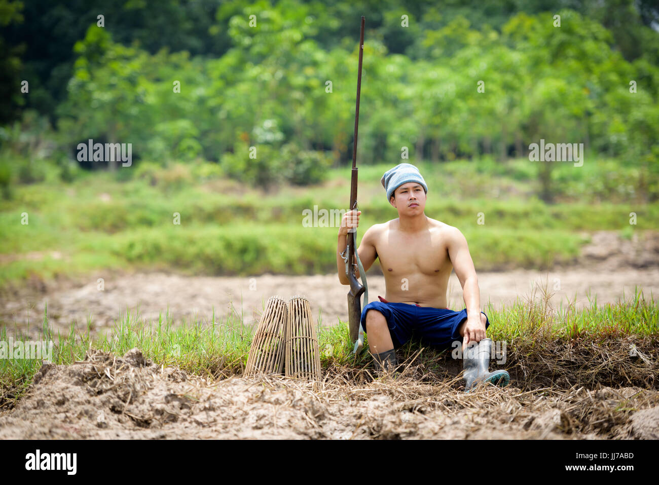 Männliche Bauer hält eine Gewehr sitzend auf einem Rasen. Stockfoto