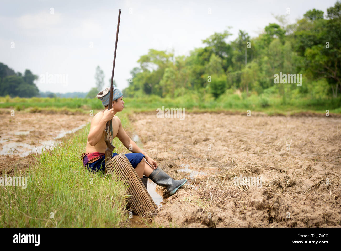 Männliche Bauer hält eine Gewehr sitzend auf einem Rasen. Stockfoto