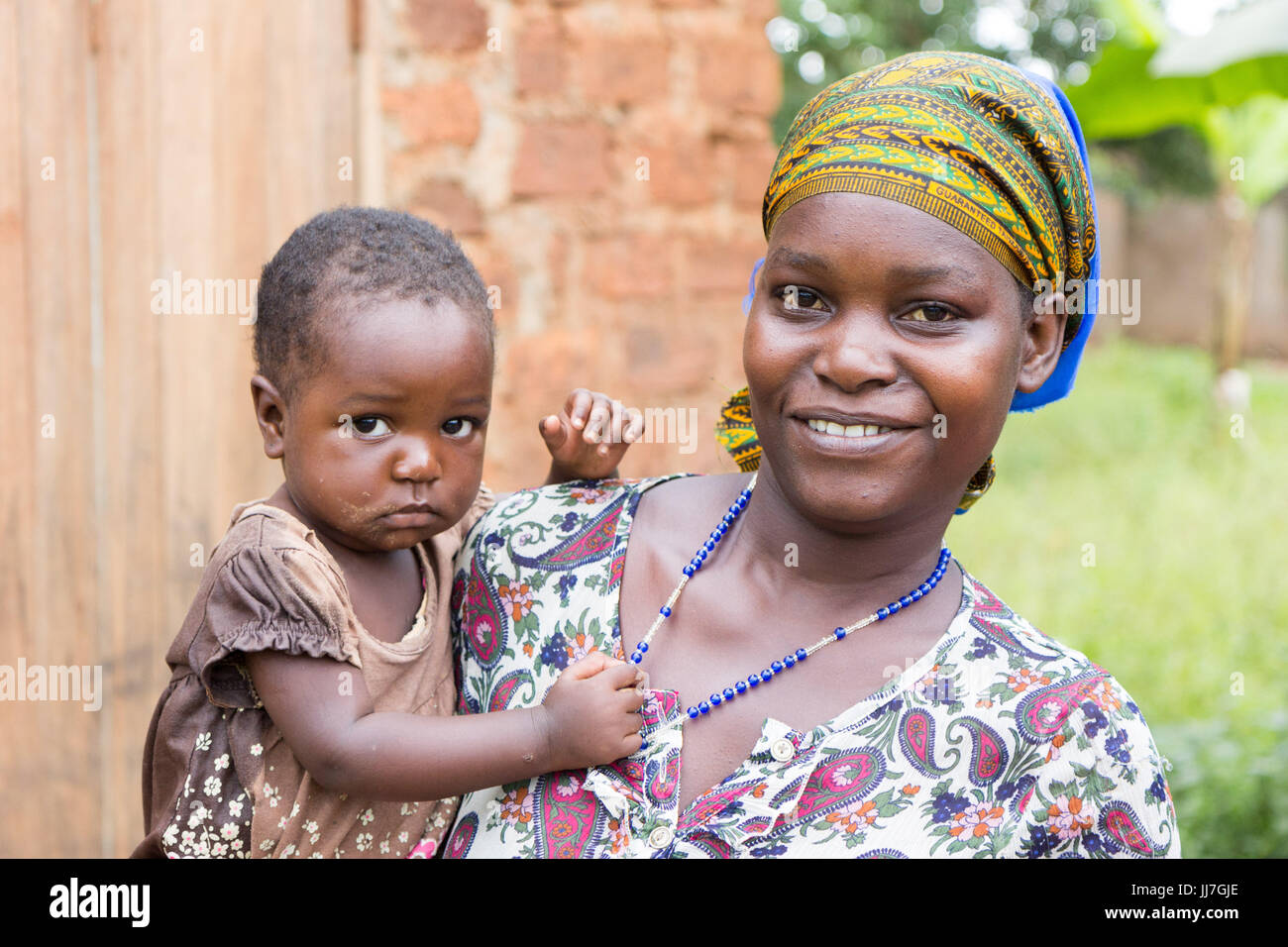 Eine glückliche ugandischen Mutter lächelnd und hält ein niedliche, einjährige Kind in die Arme Stockfoto