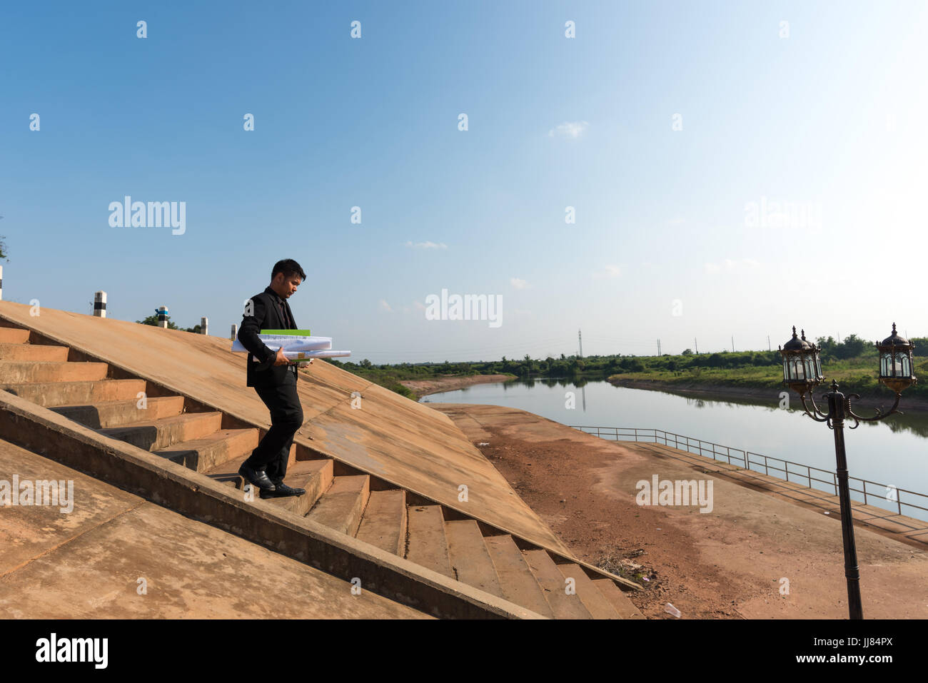 Asiatische junge Ingenieure halten eine Blaupause. Beim gehen die Treppe hinunter in die Schleusen für den Fortschritt der Überprüfung des Bauvorhabens. In Stockfoto