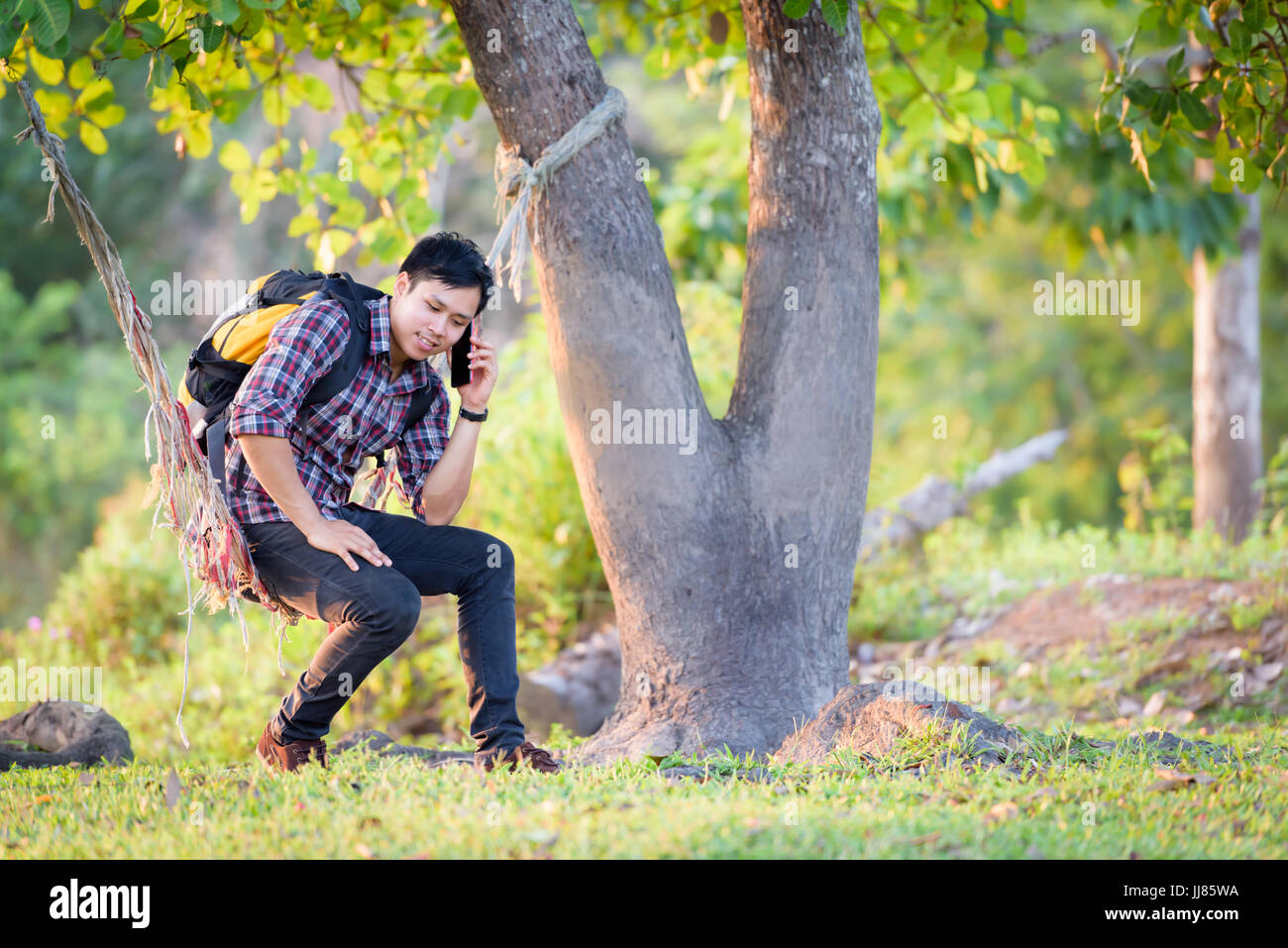 Touristen fahren auf einer Hängematte während der Benutzung eines Mobiltelefons unter einem Baum. Stockfoto