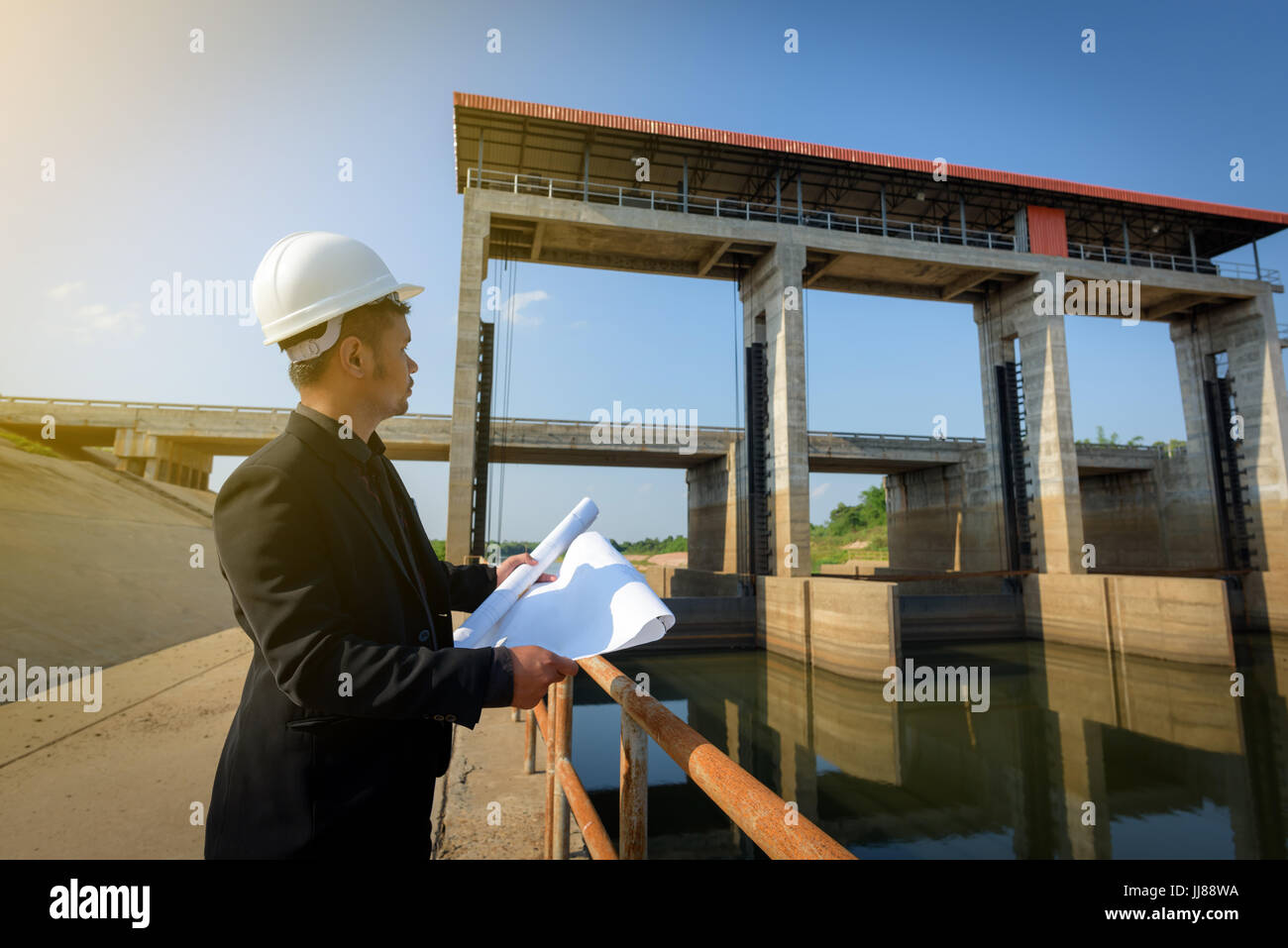 Asiatische junge Ingenieure halten eine Blaupause und mit Blick auf die Schleusen für Check Fortschritt des Bauvorhabens. Industrie und Wirtschaft Stockfoto