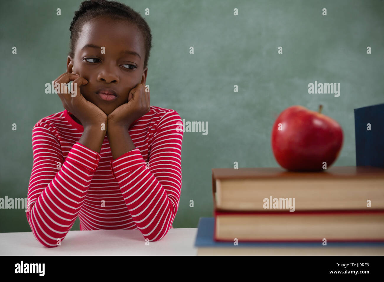 Nachdenklich Schulmädchen sitzen neben Büchern Stack gegen Tafel Stockfoto