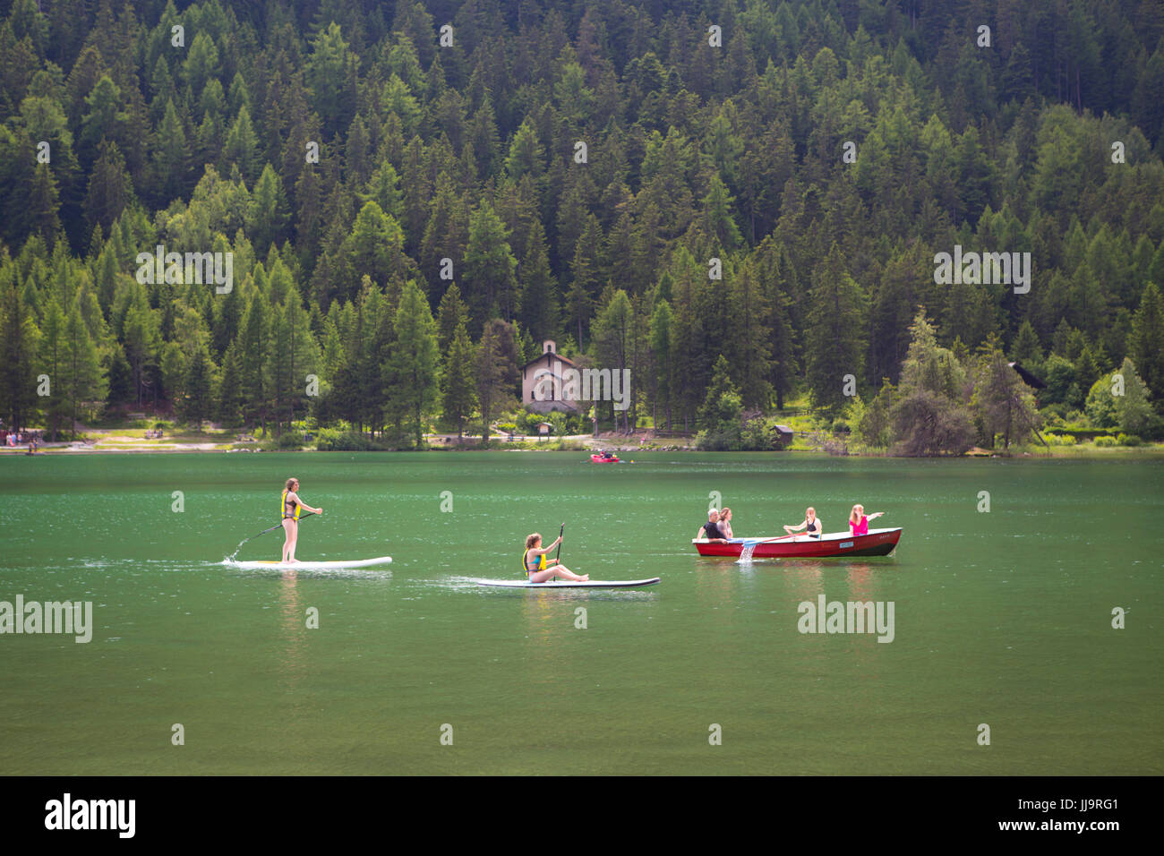Kinder in Booten und auf Surf-Brettern spielen am See Champex in den Schweizer Alpen. Stockfoto