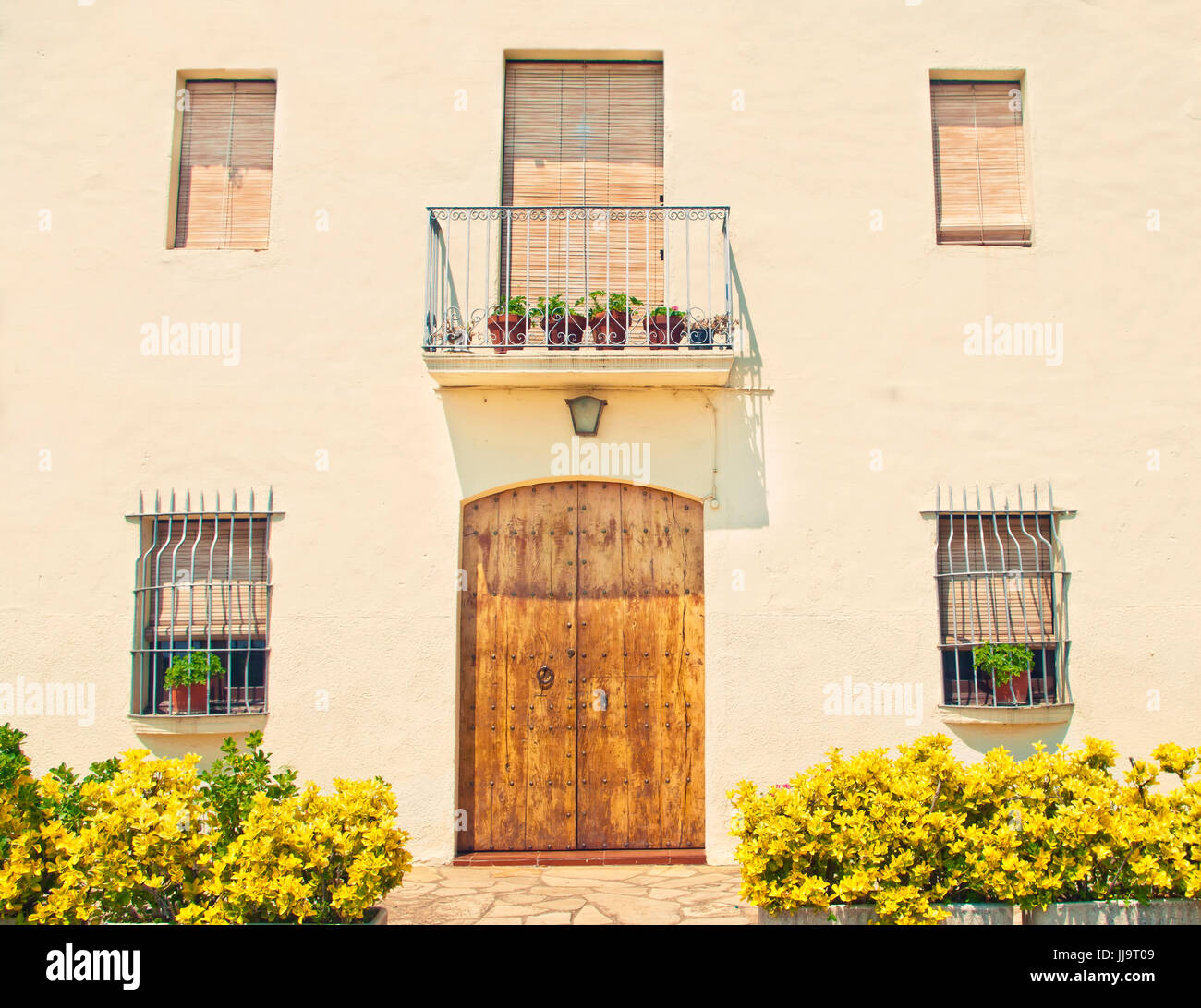 Kreuz-bearbeitetes Bild des typischen europäischen Hausfassade mit altmodischen hölzernen Tür, Fenstern und Pflanzen in Töpfen an sonnigen Sommertag, Spanien Stockfoto