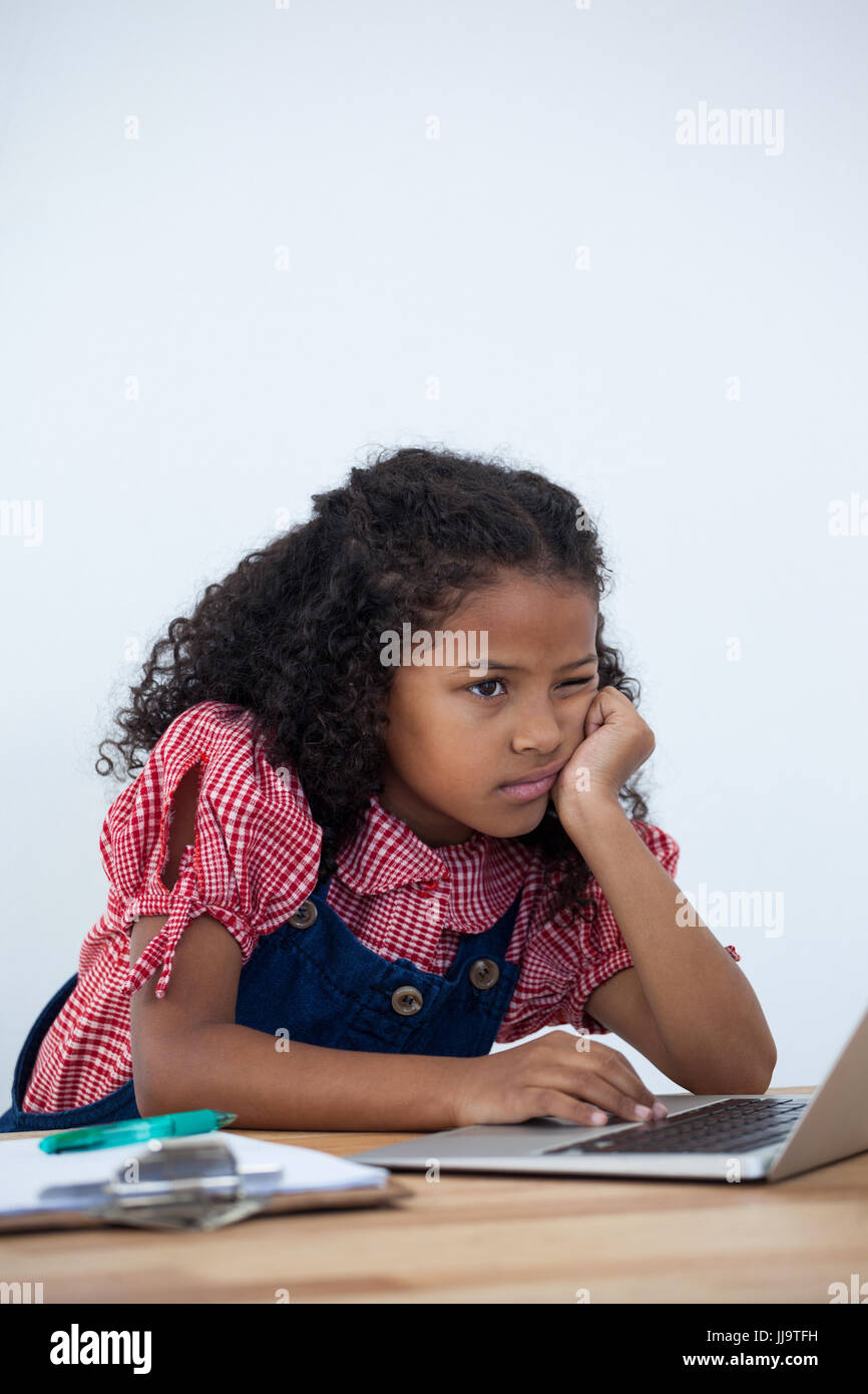 Gelangweilte Geschäftsfrau mit Hand am Kinn mit Laptop am Schreibtisch vor Whtie Hintergrund Stockfoto