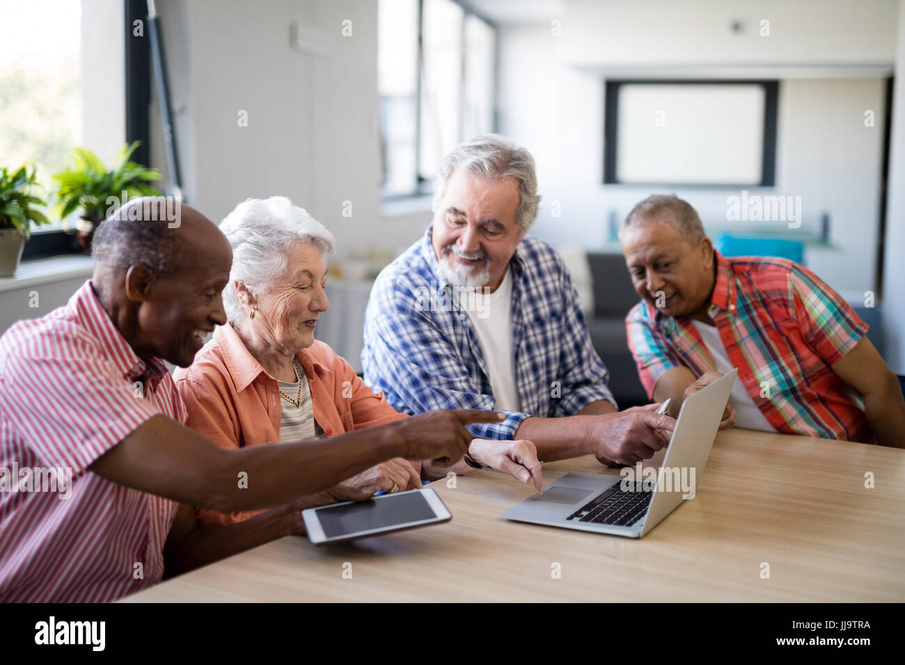 Glückliche ältere Männer und Frau mit Laptop sitzend am Tisch im Pflegeheim Stockfoto