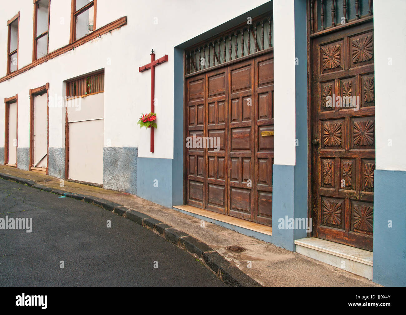 spanische Straße mit großen Holzkreuz und rote Blumen auf alten weißen Gebäudewand mit großen Holztüren, La Orotava, Teneriffa, Kanarische Inseln, Spanien Stockfoto