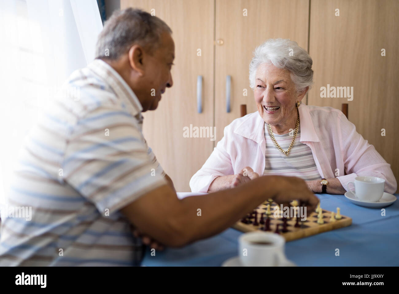 Lächelnde männlichen und weiblichen Senioren spielen Schach am Tisch im Pflegeheim Stockfoto