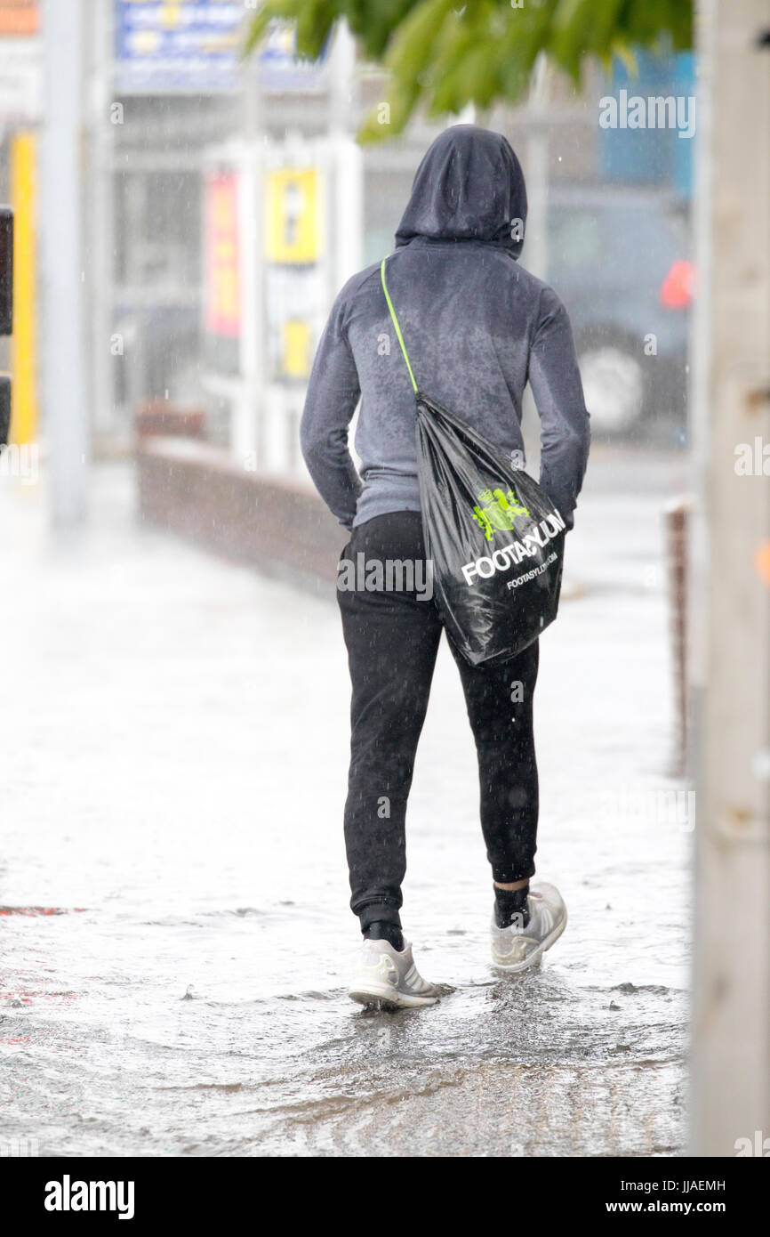 Ein Mann geht durch Flash-Überschwemmungen Wasser auf dem Heimweg nach Starkregen verursachte Sturzfluten, die A525 im Sommer während der Donner und Gewitter, die das Gebiet, Rhyl, North Wales, UK Stockfoto