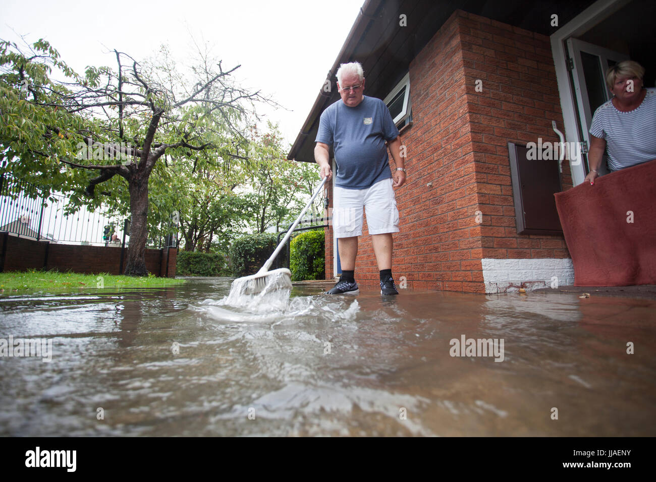 Ältere Person, die versucht, sein Haus durch Bürsten sie von der Haustür entfernt, nach Starkregen Flash-Überschwemmungen in Teilen von Nord-Wales einschließlich Rhyl links Sturzflut Wasser fernhalten Stockfoto