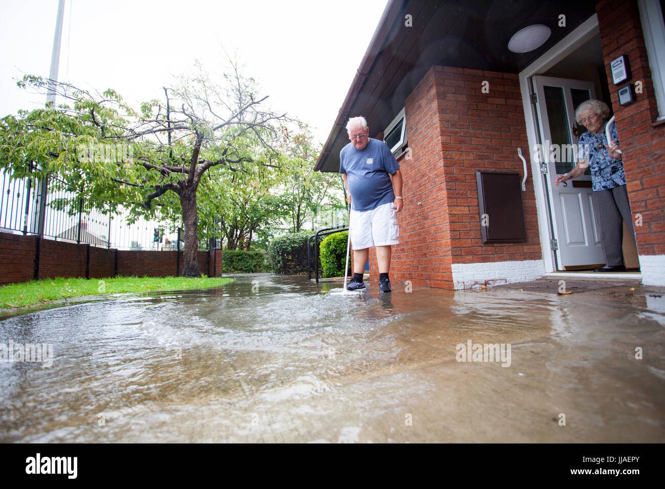 Ältere Person, die versucht, sein Haus durch Bürsten sie von der Haustür entfernt, nach Starkregen Flash-Überschwemmungen in Teilen von Nord-Wales einschließlich Rhyl links Sturzflut Wasser fernhalten Stockfoto