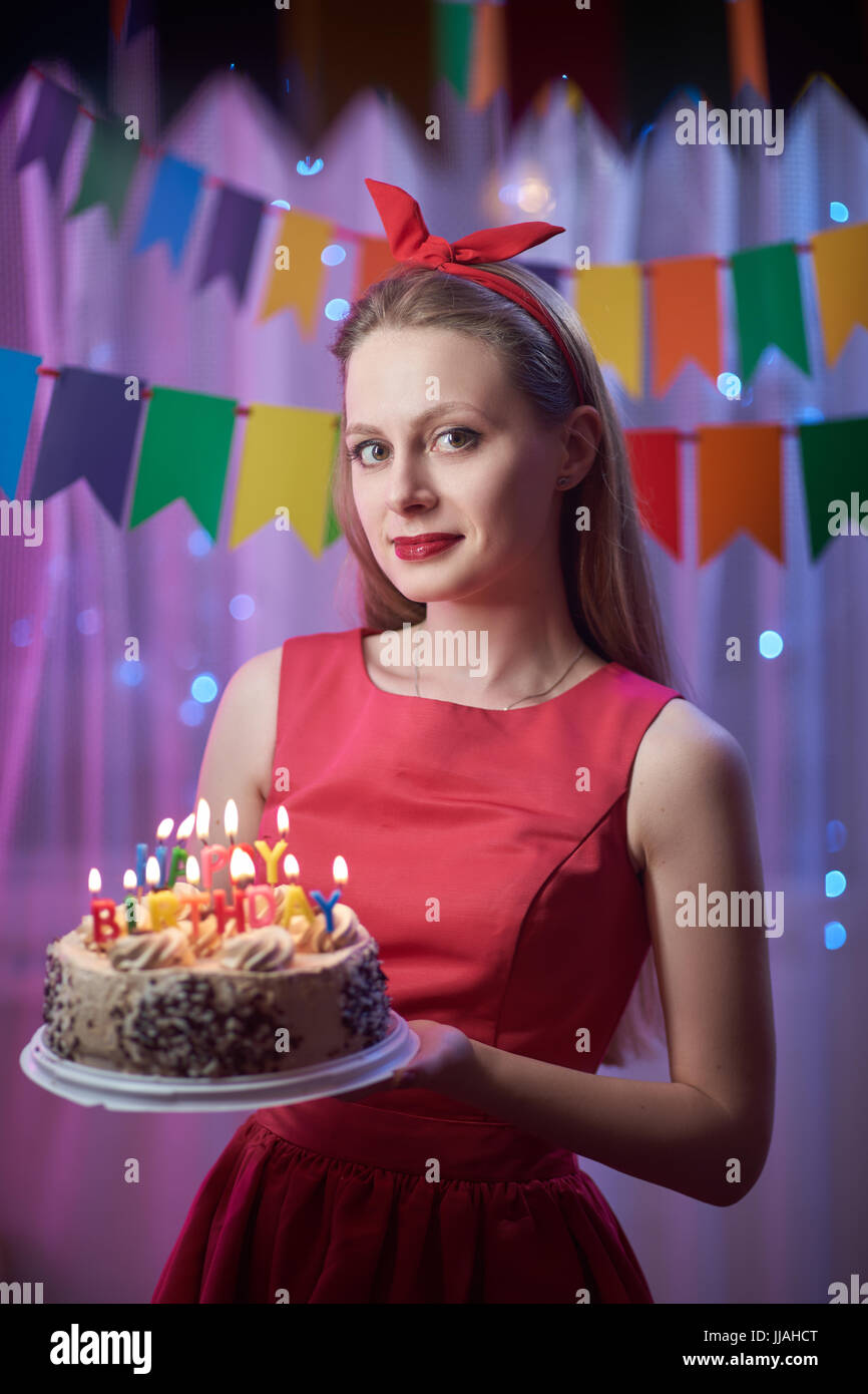 Konzept: Feier, Geburtstag. Schöne junge vintage Pin up Stil stehendes Mädchen in bunten beleuchtete Szene holding Kuchen mit Kerzen. Stockfoto