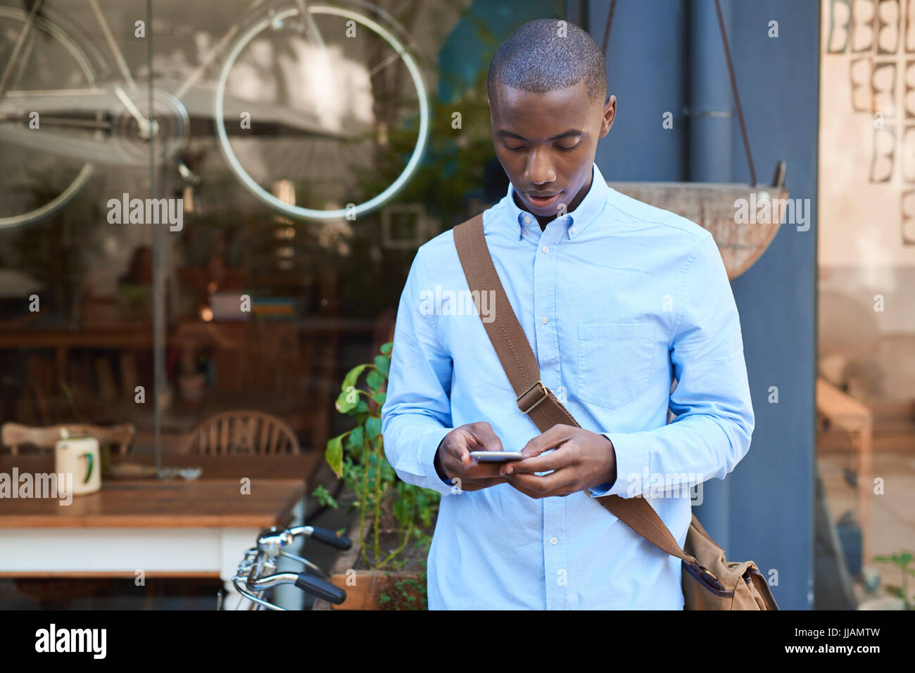 Stilvoll gekleidet junge afrikanische Mann der Straße vor einem Café lesen Text Nachrichten auf seinem Handy Stockfoto