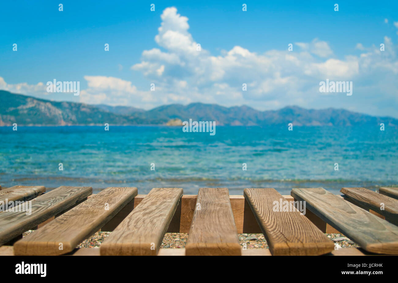 rechteckige parallelen Holzplanken liege im Vordergrund mit verwischten Meer und die Berge im Hintergrund am Kiesstrand am sonnigen Tag, Türkei Stockfoto