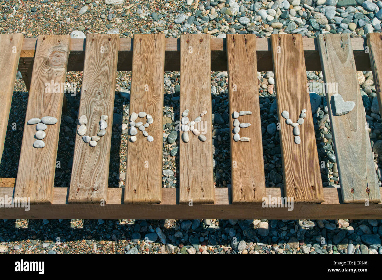 Wort-Türkei gesäumt mit kleinen Kieselsteinen auf hölzernen Liegestuhl mit herzförmigen Stine am Kiesstrand, Marmaris, Türkei Stockfoto