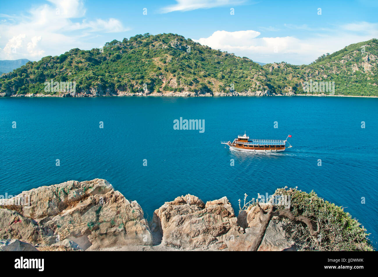 Blick auf Bucht der Ägäis mit Touristenboot aus Felsen mit grünen Bergen im Hintergrund am sonnigen Tag, Marmaris, Türkei Stockfoto