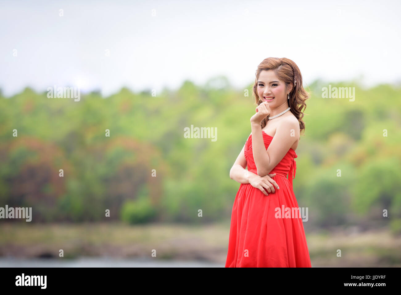 Schöne Frau tragen rote Abendkleid über Berge und Flüsse Hintergrund. Stockfoto