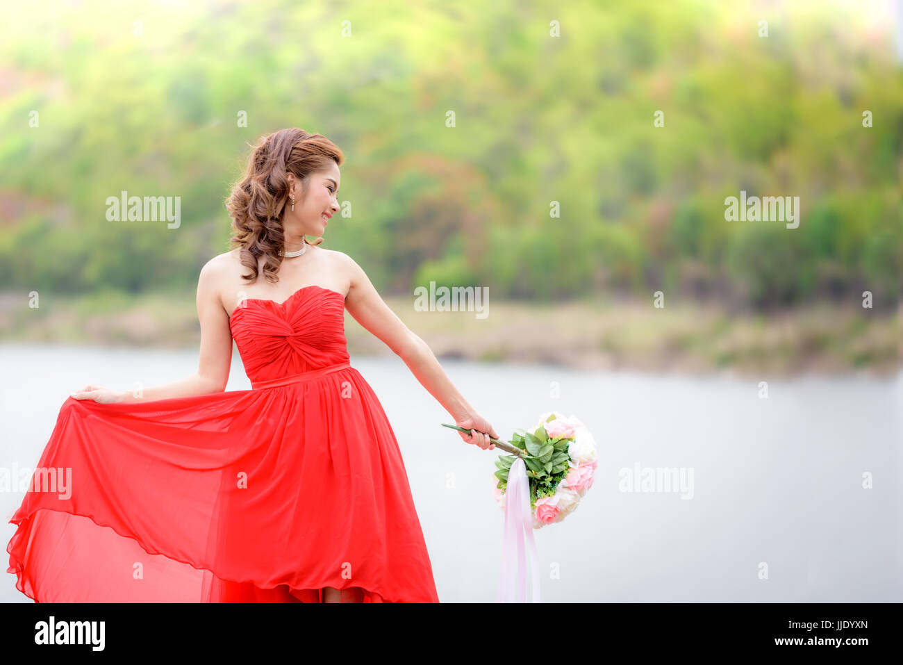 Schöne Frau tragen rote Abendkleid halten einen Blumenstrauß. über Berge und Flüsse Hintergrund. Stockfoto