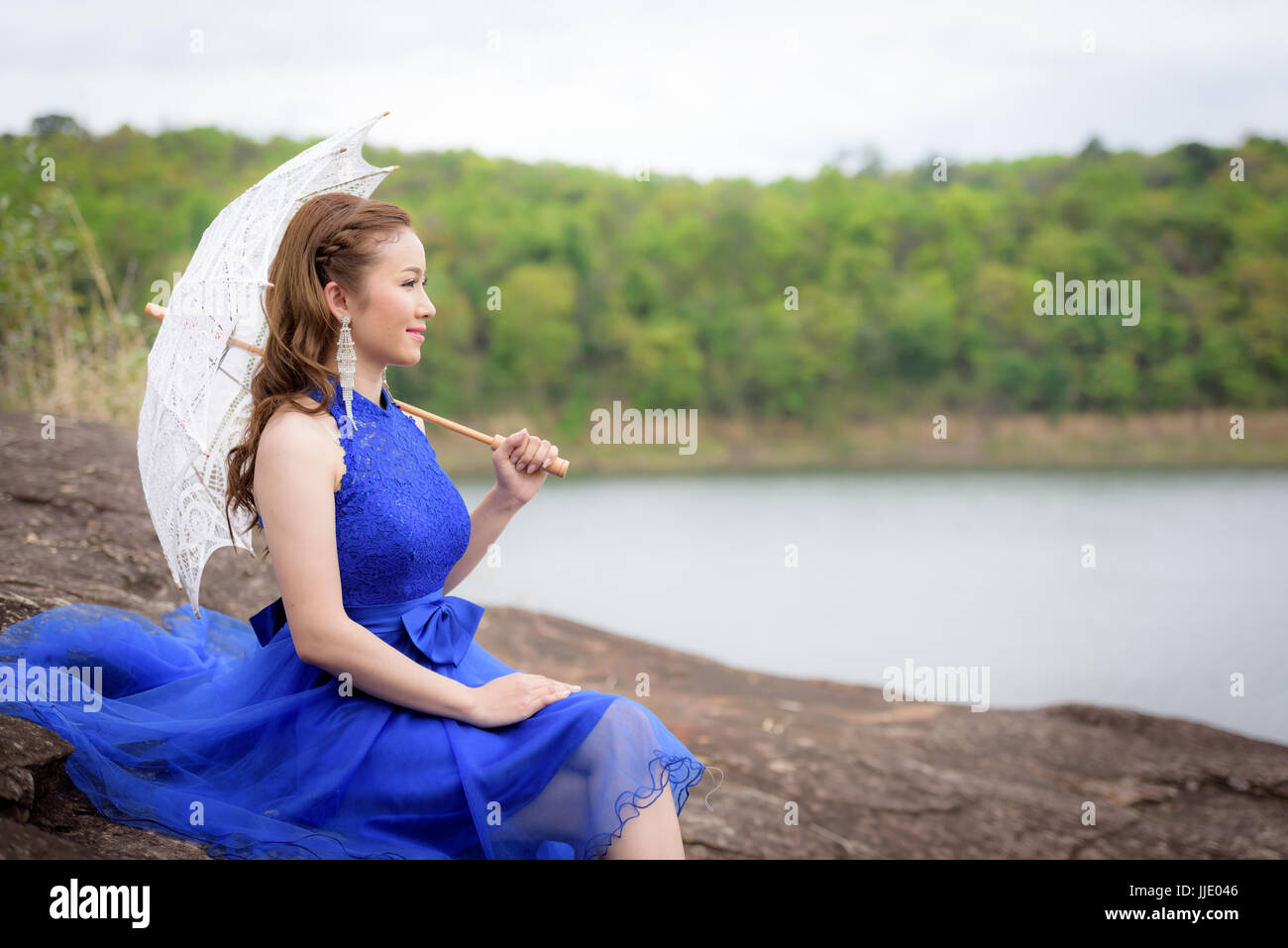 Schöne Frau tragen blaue Abendkleid halten weißen Schirm, den Blick auf den Felsen beobachten. Stockfoto