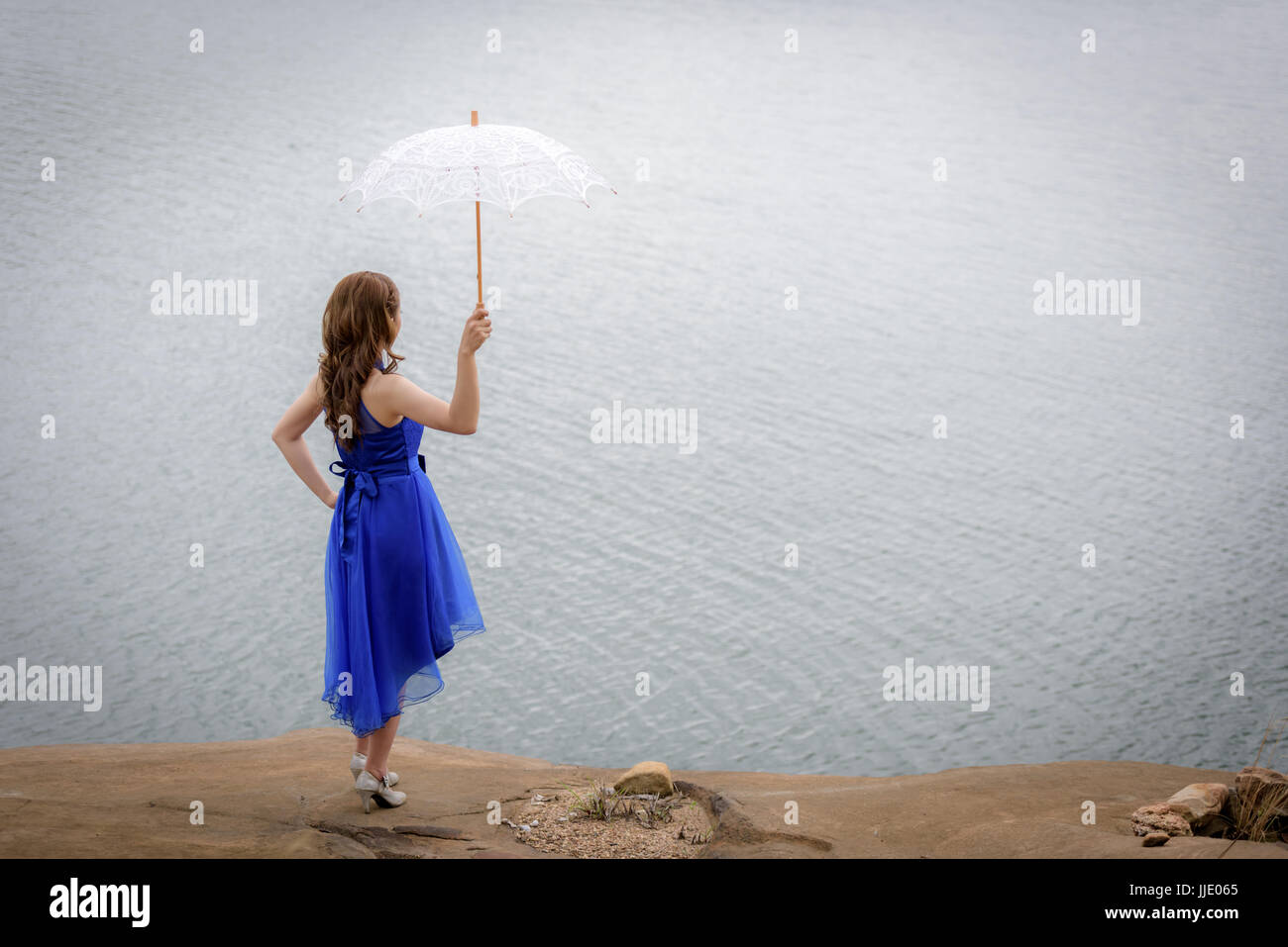 Schöne Frau tragen blaue Abendkleid halten weißen Schirm, den Blick auf den Felsen beobachten. Stockfoto