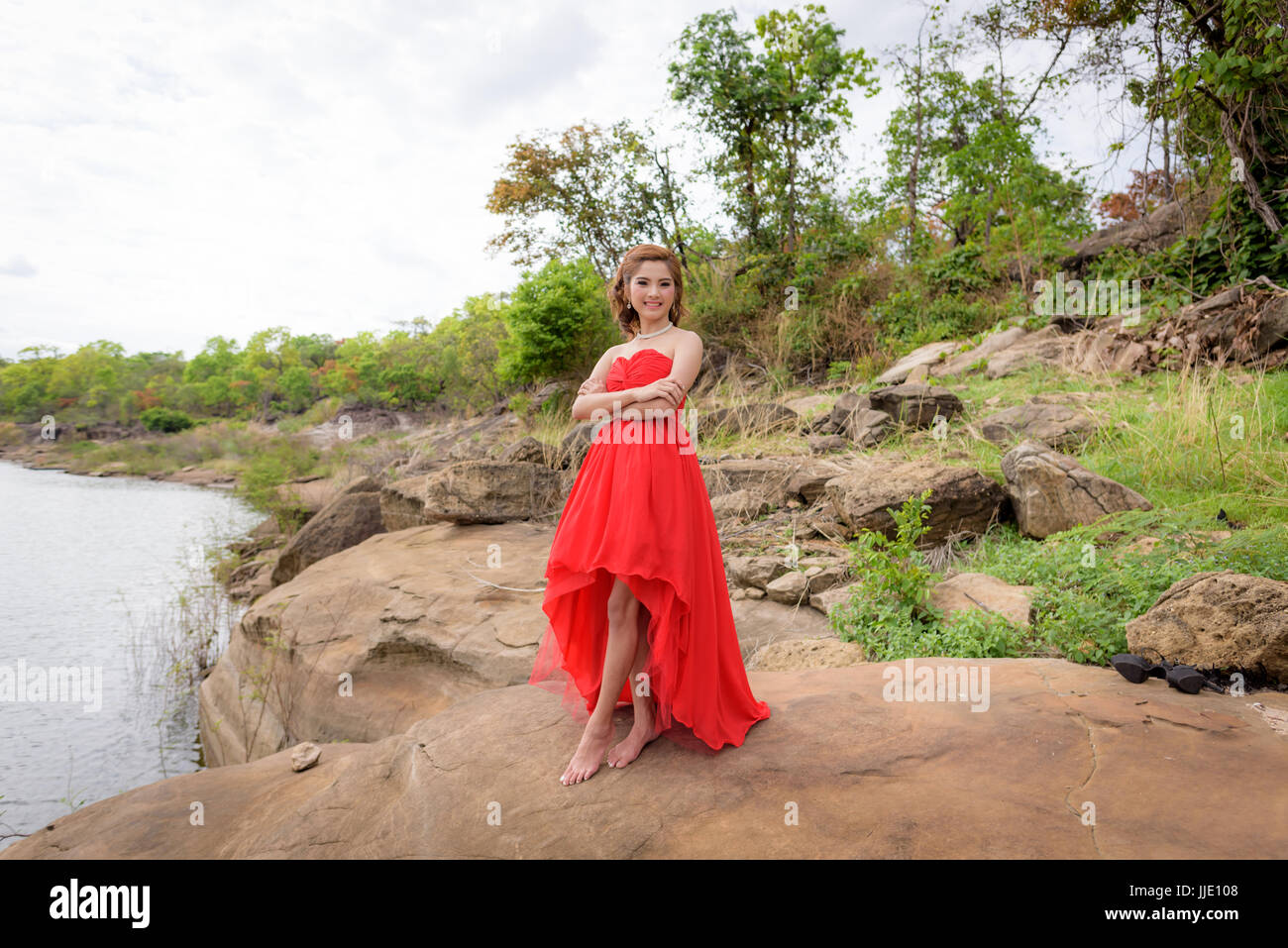 Schöne Frau tragen rote Abendkleid über Berge und Flüsse Hintergrund. Stockfoto