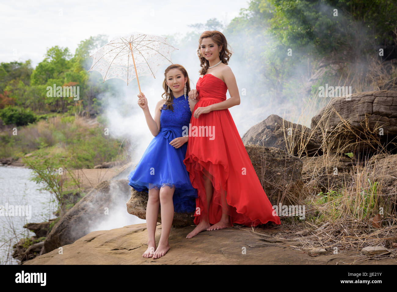 2 junge Frauen tragen blaue und rote Kleider halten weiße Sonnenschirme beobachten Fluss und die Berge. Stockfoto