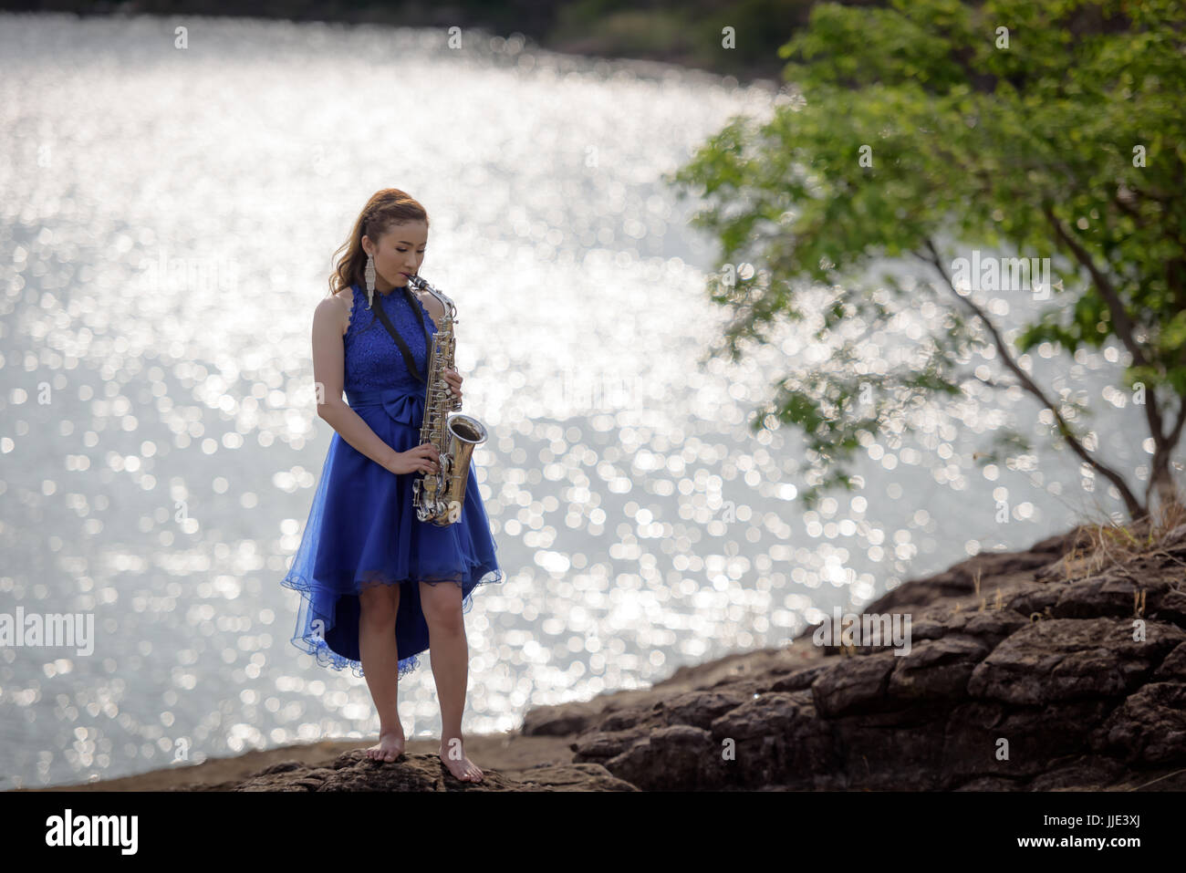 Schöne Frau tragen blaue Abendkleid sound Saxophon Ständer auf den Felsen über Berge und Flüsse Hintergrund. Stockfoto