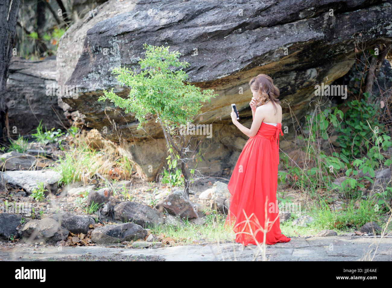 Schöne Frau tragen rote Abendkleid sprechende Handy im Dschungel. Stockfoto