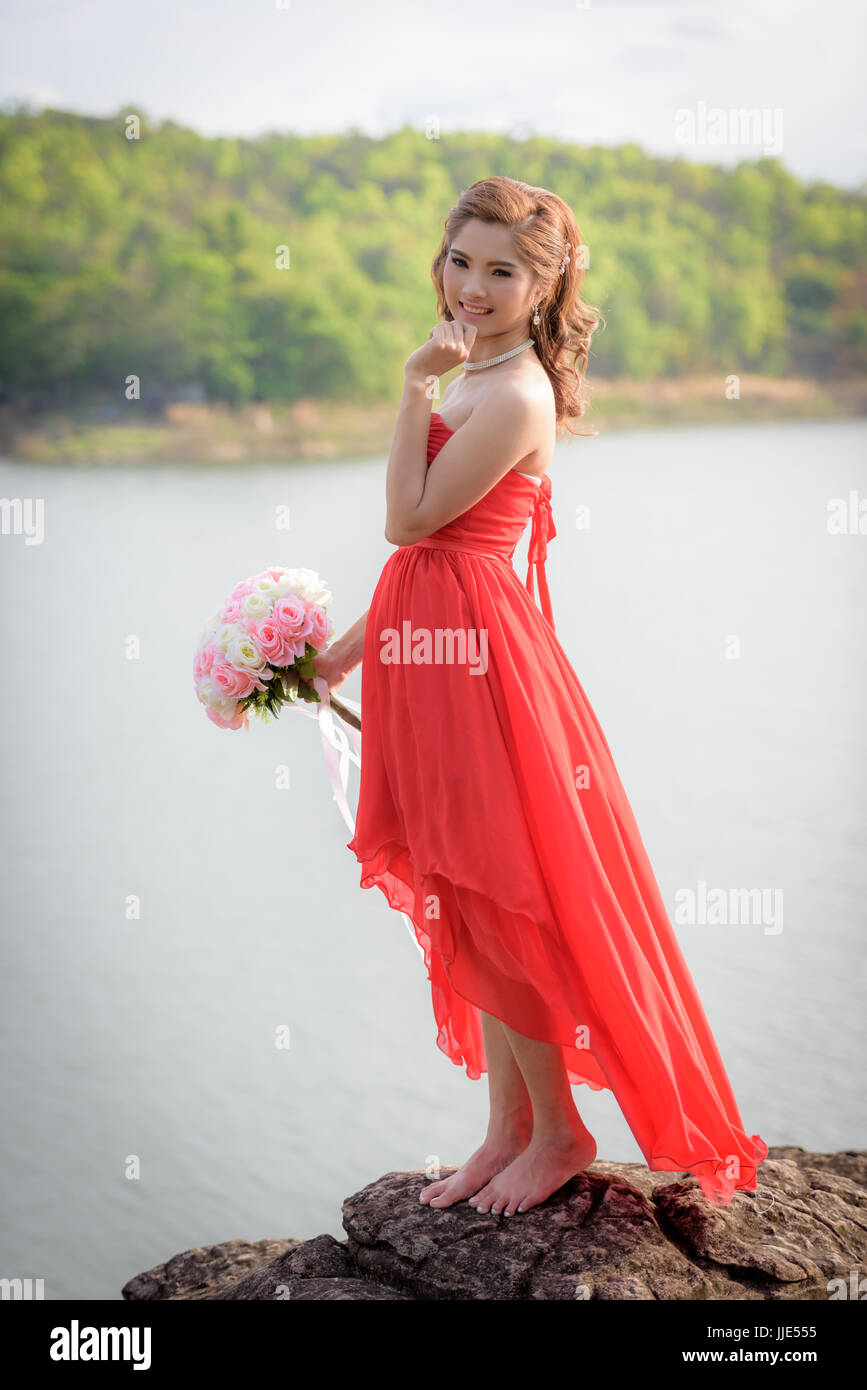 Schöne Frau tragen rote Abendkleid halten einen Blumenstrauß. über Berge und Flüsse Hintergrund. Stockfoto