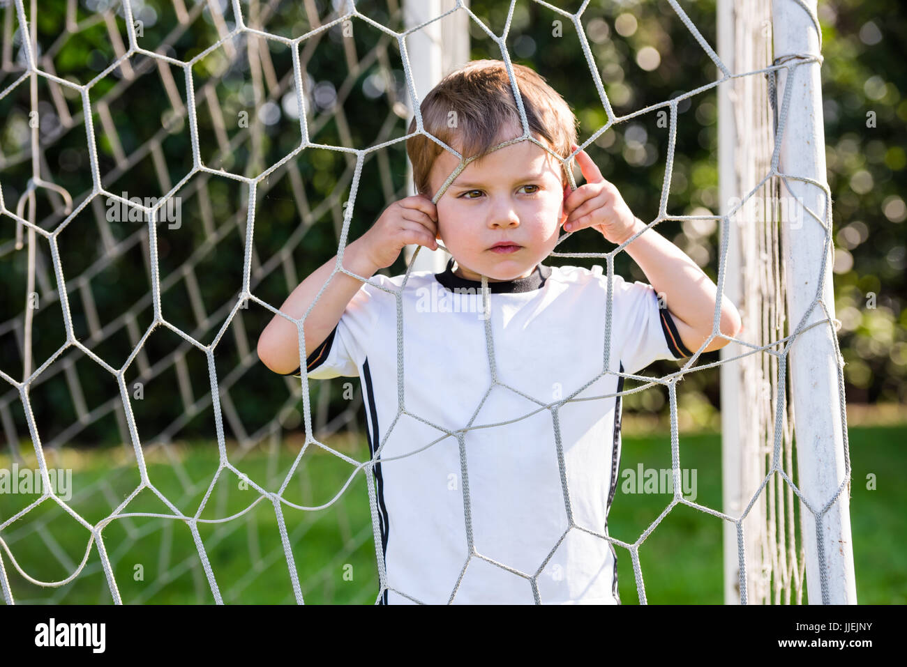 Kind, das auf dem Fußballfeld durch das europäische Fußballnetz schaut Stockfoto