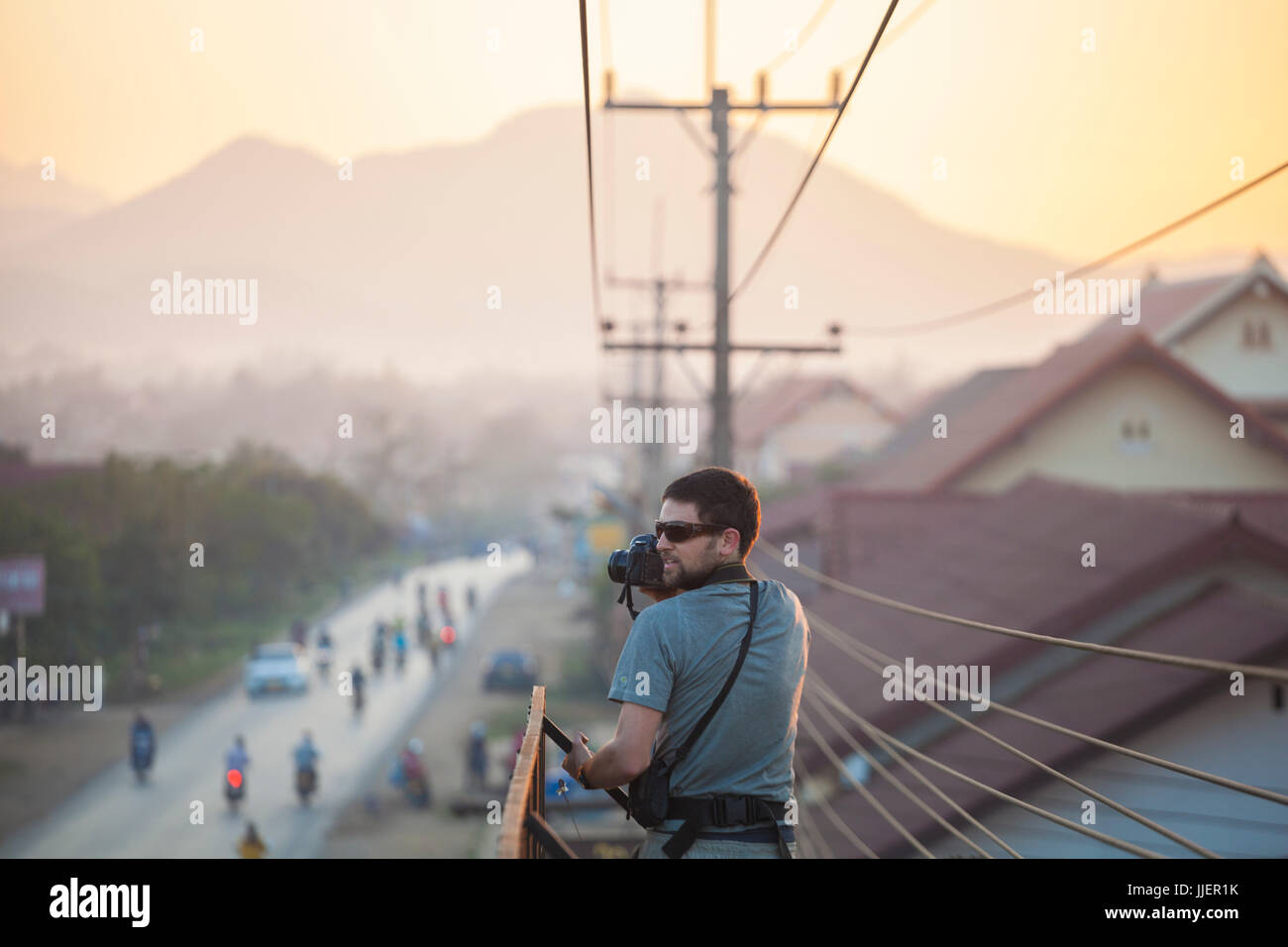 Robert Hahn nimmt Bilder an einer belebten Straße bei Sonnenuntergang von der Spitze einer Plakatwand in Luang Prabang, Laos. Stockfoto
