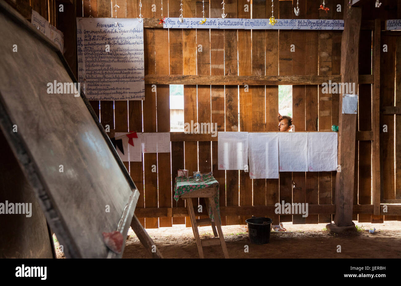 Ein kleiner Junge schaut in einen verschlossenen Raum ein Schulhaus in Ban Tang, Laos während der Winterpause. Stockfoto