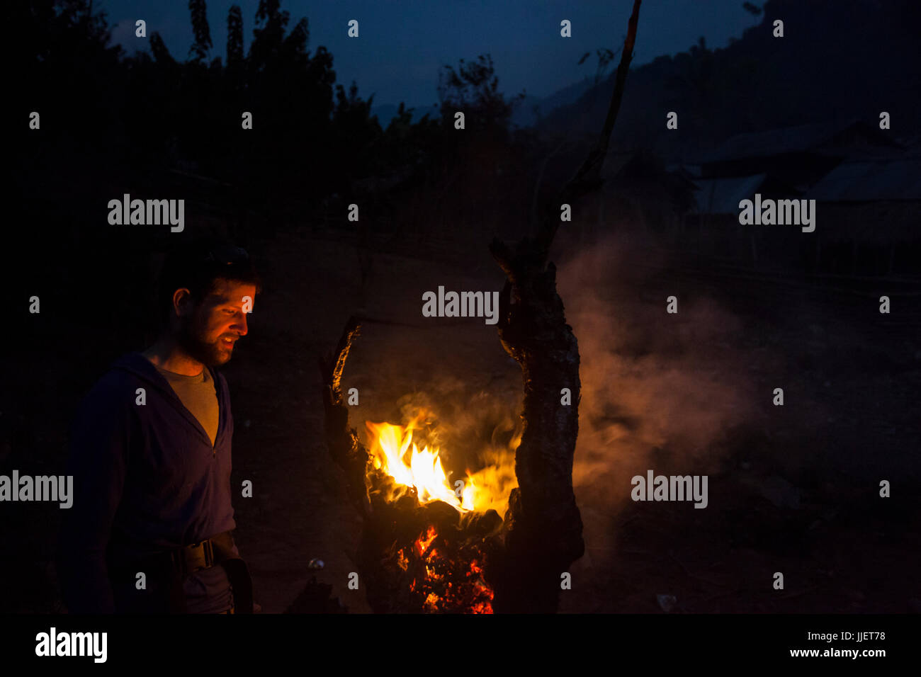 Robert Hahn schaut in ein Feuer in einem Baumstumpf am Stadtrand von Muang Hut Hin, Laos. Stockfoto