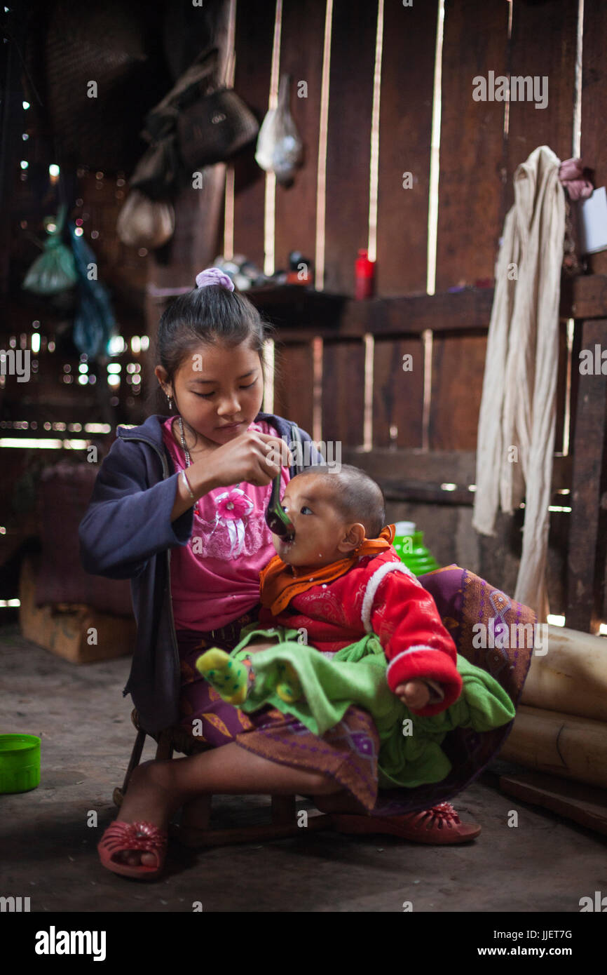 Ein Mädchen-Löffel füttert ihr Baby Bruder in ihrem Haus in Muang Hut Hin, Laos. Stockfoto