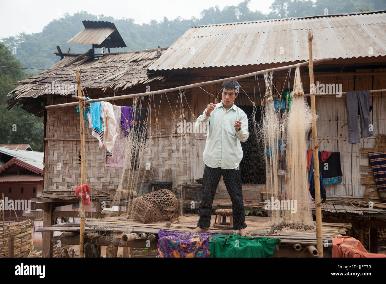 Ein Mann repariert sein Fischernetz auf seiner Veranda in Muang Hut Hin, Laos. Stockfoto