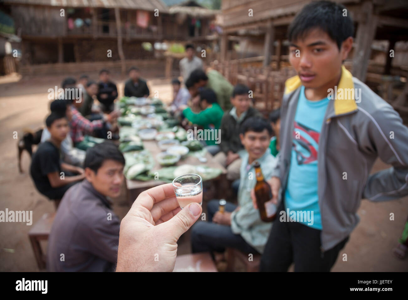 Ethan Welty führt einen Torwurf von Lao-Lao (Reis-Whisky) zu Beginn der Hochzeitsfeier in Muang Hut Hin, Laos. Stockfoto
