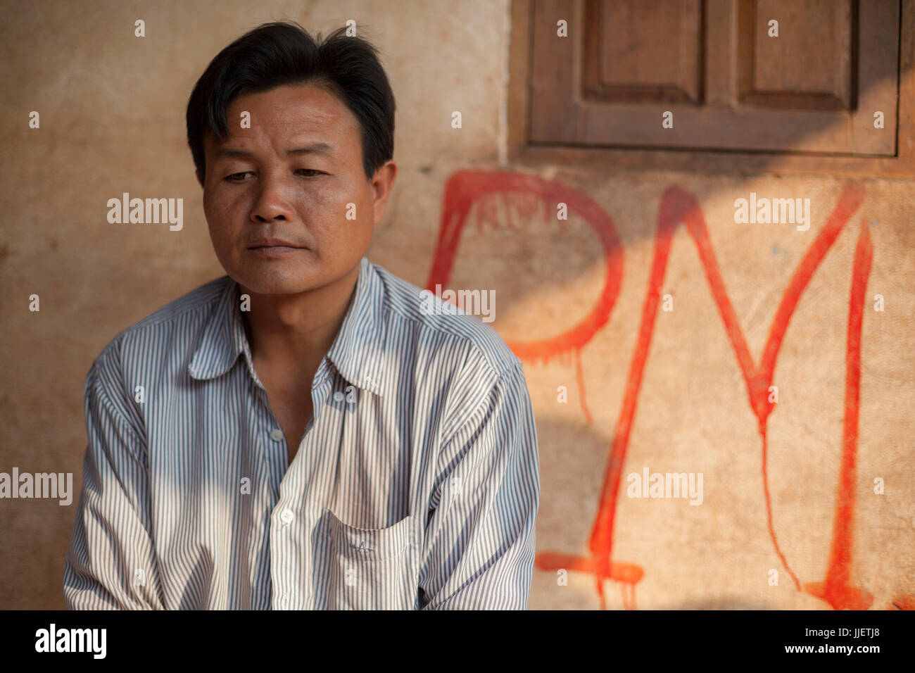 Ein Dorfhäuptling sitzt vor seinem markierten Haus in Ban Phu Muang, Laos. Die roten Markierungen wurden durch Lao Regierungsbeamte, tagging jedes Haus mit einen Ersatzwert für Entschädigung nach des Dorfes Überschwemmungen durch Nam Ou River Dam #6 gemacht. Stockfoto