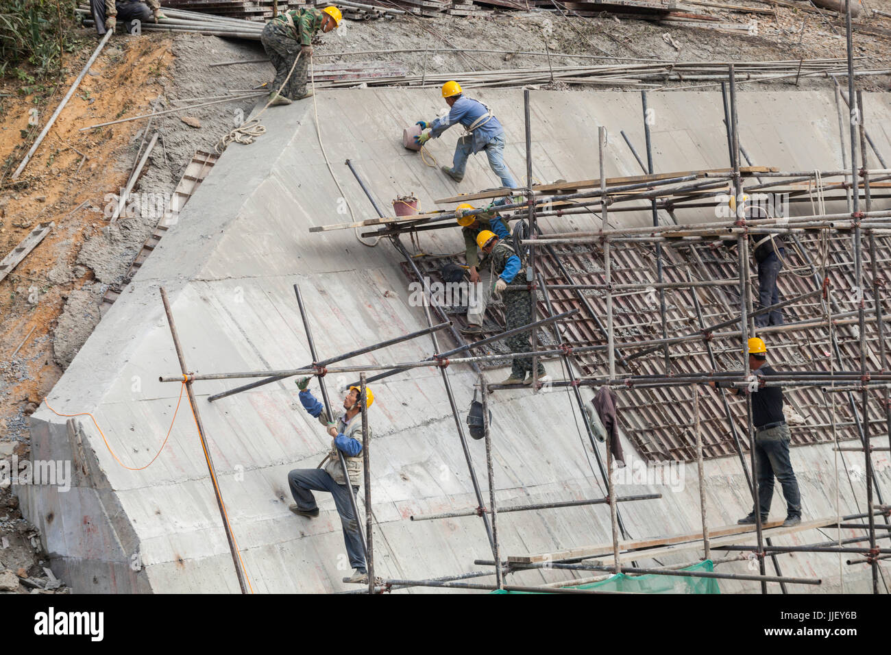 Arbeiter klettern auf Gerüste und bauen eine dicke Betonmauer an der Mündung eines großen Umlenkdamms (Box) an der Stelle des Staudamms Nr. 6 am Fluss Nam ou, Laos. Stockfoto