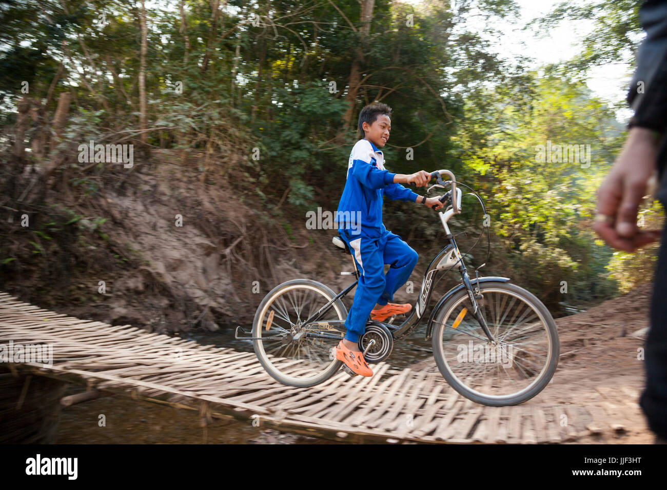 Ein Junge reitet sein Fahrrad über die geflochtenem Bambus-Brücke über den Zufluss Bach zum Fluss Nam Ou außerhalb Ban Huay Phouk, Laos. Stockfoto