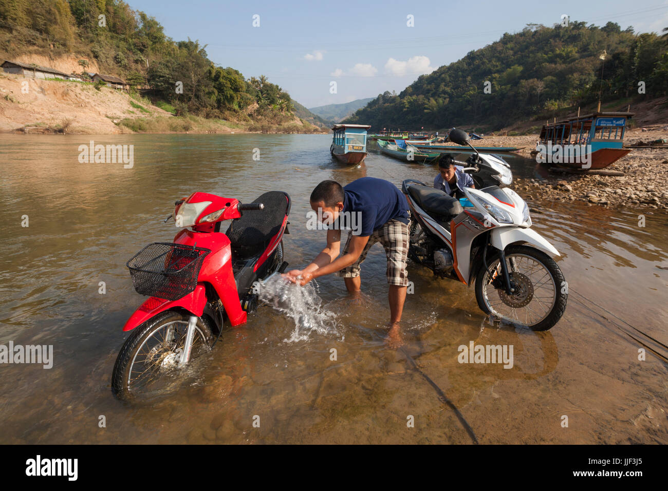 Männer spülen Sie ihren Motorroller im Fluss Nam Ou in Muang Khua, Laos. Stockfoto
