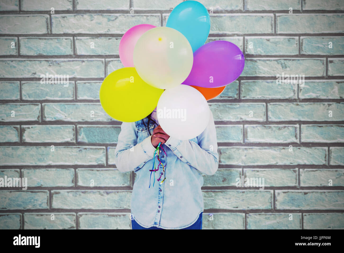Frau, verstecken ihr Gesicht mit Haufen von bunten Luftballons gegen eine Steinmauer Stockfoto